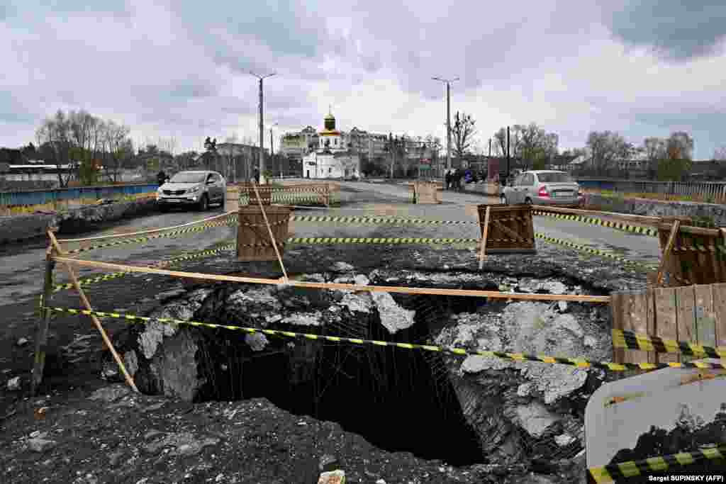 Cars drive past huge holes on a damaged bridge in Makariv, outside Kyiv.