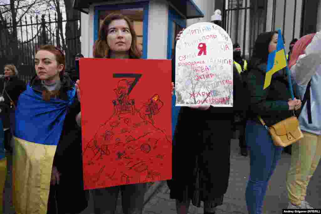 Woman stand in silent protest while one of them holds a placard with the names of places that have suffered under Russian occupation or attack.