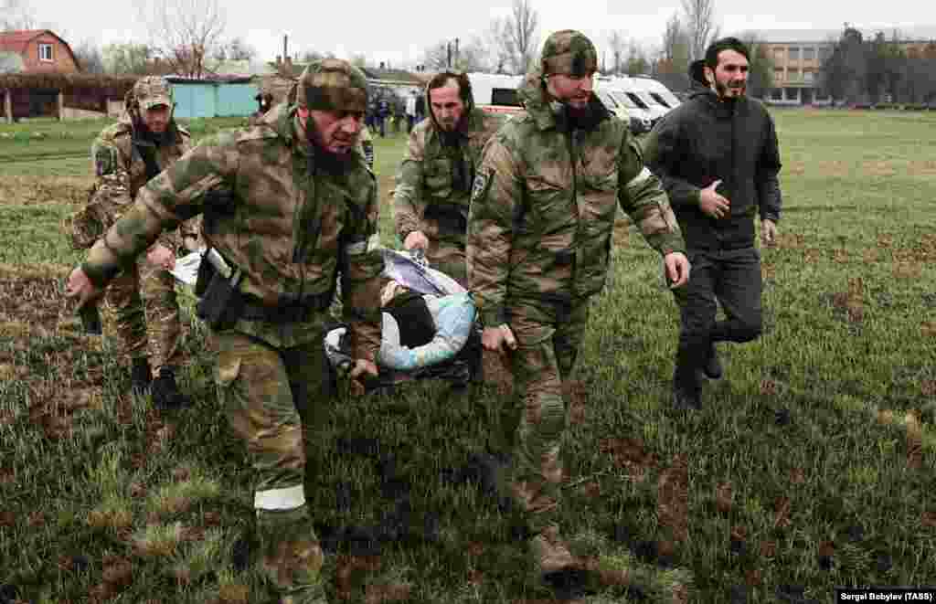 Военные из российского региона Чечня уносят раненого с поля боя в Новоазовске, 12 апреля