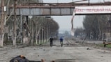 Two people on bicycles and a dead body on devastated street in Mariupol_Ukraine