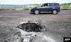 Автомобіль проїжджає повз воронку на Антонівському мосту в Херсоні через річку Дніпро, спричинену, як повідомляють, ударом ЗСУ. Херсон, 21 липня 2022 року