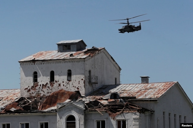 Soğıs kesirinen qirağan üylerdiñ üstinen wşıp bara jatqan reseylik äskeri tikwşaq. Popasnaya qalası, Lugansk oblısı, Ukraina, 2 mausım 2022 jıl.