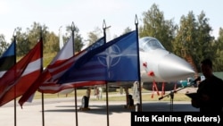 Steagurile NATO, SUA, Poloniei și ale Letoniei în fața unui avion de vânătoare F-15C Eagle, în timpul ceremoniei de predare a misiunii NATO de patrulare aeriană în Țările Baltice. (fotografie de arhivă)