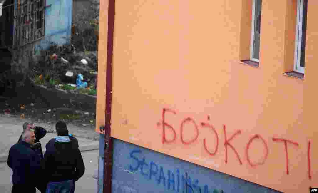 A group of ethnic Serbs stand near graffiti in Mitrovica calling for an election boycott.