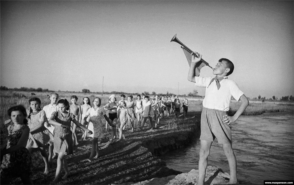 A young Pioneer trumpets the march of youngsters along a riverbank.