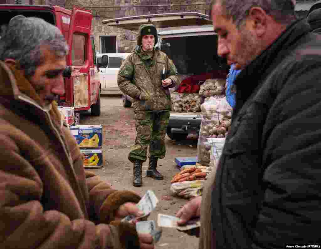 Locals exchange money as a Russian soldier waits to complete a purchase in Gyumri&#39;s central market. Russian servicemen are a common sight, with an estimated 3,000 Russian soldiers stationed in the city of 120,000, and many travel to the city center on breaks and shopping runs.