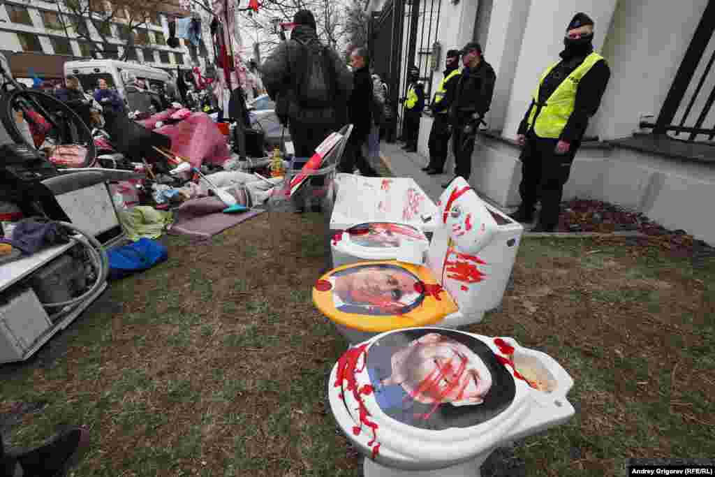 Police stand guard at the Russian Embassy gate as mounds of items are placed there by protestors.