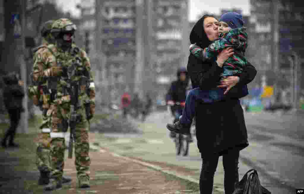 A woman carrying a child passes Russian soldiers on the street in the besieged port city of Mariupol, Ukraine.