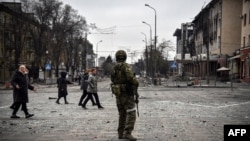 People walk past a Russian soldier in central Mariupol on April 12.