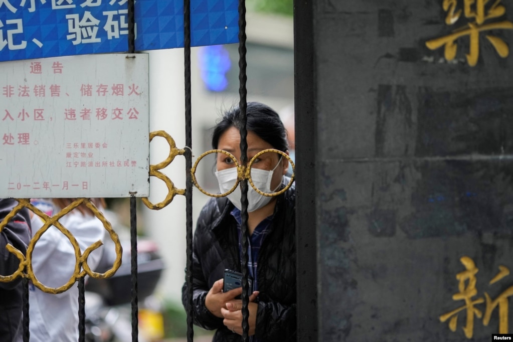 Një banor i Shangait duke pritur shpërndarjen e ushqimit pas një porte të mbyllur që bllokon hyrjen në zonën e banimit për shkak të përhapjes së Omicronit, variantit tejet ngjitës të COVID-19, 13 prill 2022.