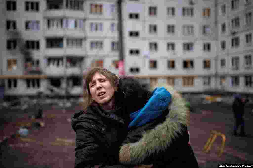 Две жени плачат во дворот на станбен комплекс во Харков кој беше погоден од артилерија на 13 април.