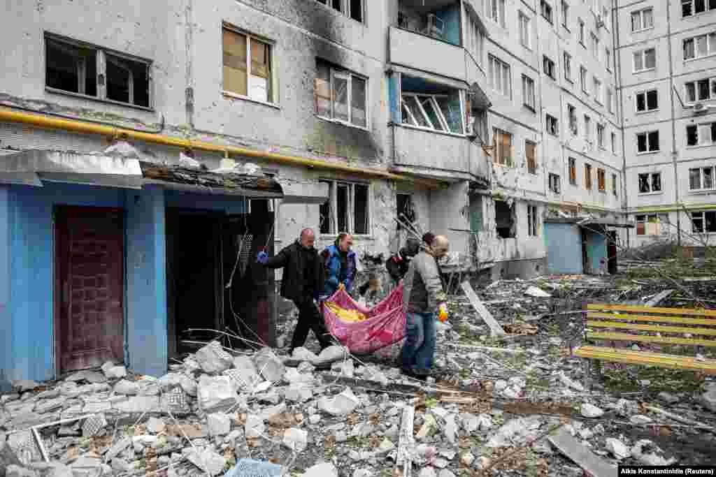 Вработени во итната помош отстрануваат тело на една жена по артилерискиот напад кој оштети станбен блок во Харков на 13 април.