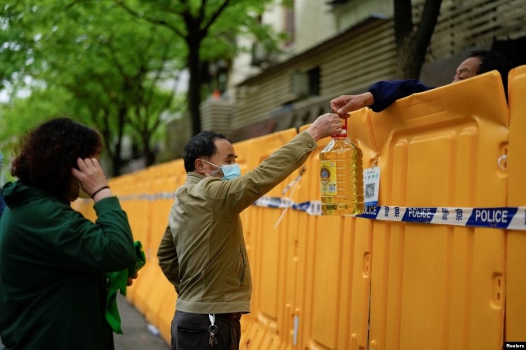 Njerëzit duke bartur vaj gatimi sipër barrierave të vendosura në një rrugë për shkak të masave kufizuese si pasojë e përhapjes së COVID-19, Shangai, 13 prill 2022.