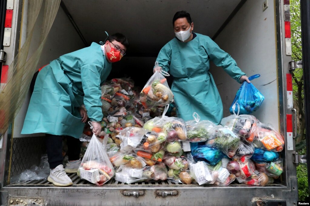 Punëtorët me maska mbrojtëse sistemojnë qese me perime dhe gjëra ushqimore në një kamion që u dërgon ushqim banorëve në pjesët e mbyllura të Shangait, prill 2022.