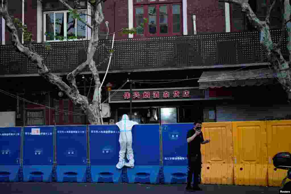 Një person i veshur me veshje mbrojtëse kundër koronavirusit duket teksa është zgjatur mbi barrikadën e ngritur për të mbyllur plotësisht një pjesë të qytetit të Shangait si pjesë e masave të rrepta të kufizimit nga përhapja e koronavirusit, prill 2022.
