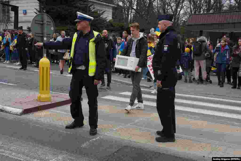 Polish police stop traffic to allow a man carrying a microwave to cross the road. Protestors were encouraged to bring household goods to mock alleged thievery by Russian troops in Ukraine.