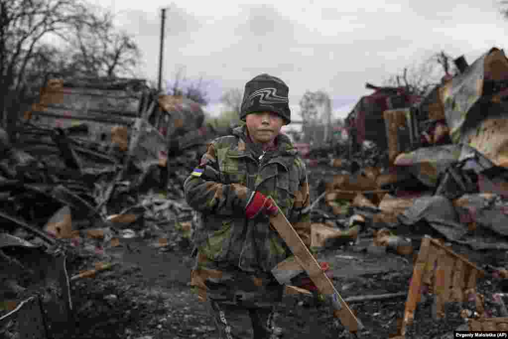 Yehor, 7, stands holding a wooden toy rifle next to destroyed Russian military vehicles near Chernihiv, Ukraine.