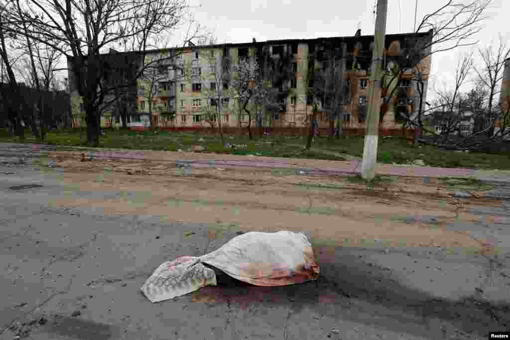 Egy civil holtteste letakarva Mariupol egyik utcáján április 18-án