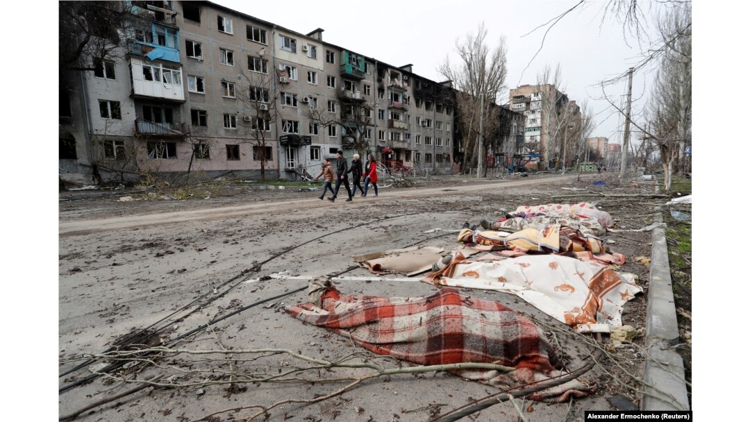 Câțiva locuitori ai Mariupolului trec pe lângă cadavrele unor persoane, pe o stradă din orașul asediat de la începutul invaziei ruse, 17 aprilie 2022.
