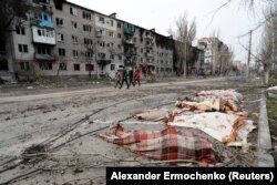 Câțiva locuitori ai Mariupolului trec pe lângă cadavrele unor persoane, pe o stradă din orașul asediat de la începutul invaziei ruse, 17 aprilie 2022.