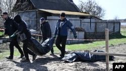 A Ukrainian policeman and municipal workers carry a body bag as they exhume two bodies from graves dug in the yard of a house in the village of Vabliya, near Kyiv, on April 14.