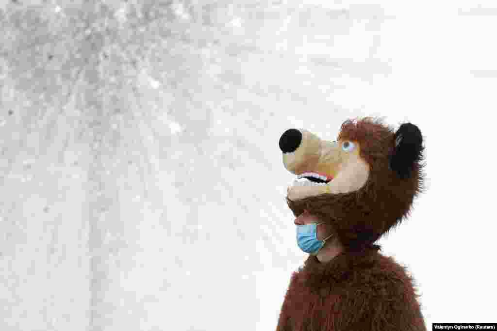 A man dressed as a bear and wearing a protective face mask stands in front of a fountain in central Kyiv. (Reuters/Valentyn Ogirenko)