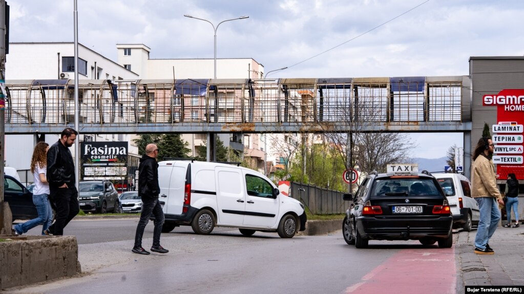 Njerëzit e kalojnë rrugën mes veturash pranë një mbikalimi të pashfrytëzuar në Fushë-Kosovë.