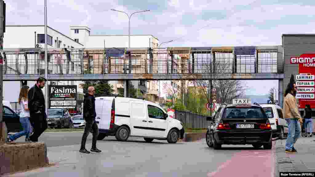 Njerëzit e kalojnë rrugën mes veturash pranë një mbikalimi të pashfrytëzuar në Fushë-Kosovë.