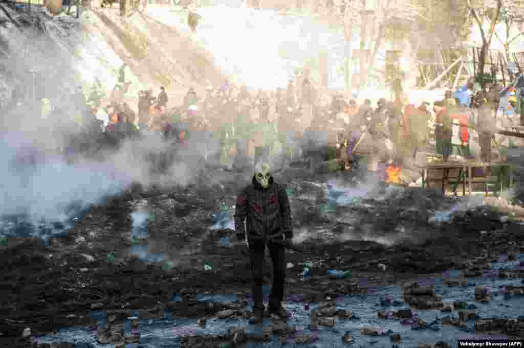 A protester wearing a gas mask walks through smoking rubble.