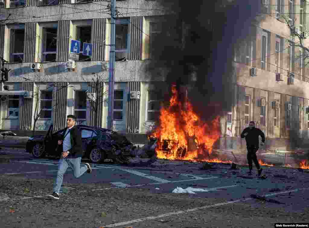 Men run from the scene of a Russian military strike as cars burn in central Kyiv on October 10.