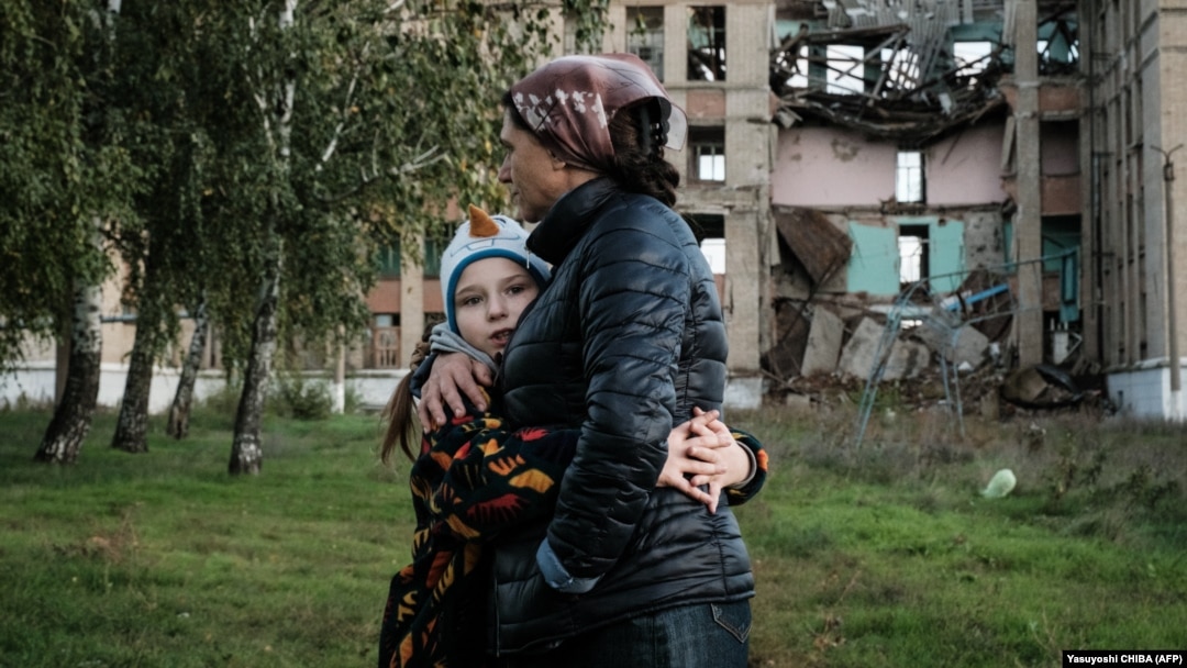 Vera (8 ani) și mama sa Olga în fața unei școli distruse din regiunea Donețk, 13 octombrie 2022.