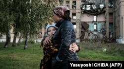 Vera (8 ani) și mama sa Olga în fața unei școli distruse din regiunea Donețk, 13 octombrie 2022.