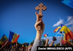 Un suporter al partidului AUR, ținând în mână o cruce cu însemne creștin-ortodoxe, la protestul din fața Guvernului României, 2 octombrie 2022.