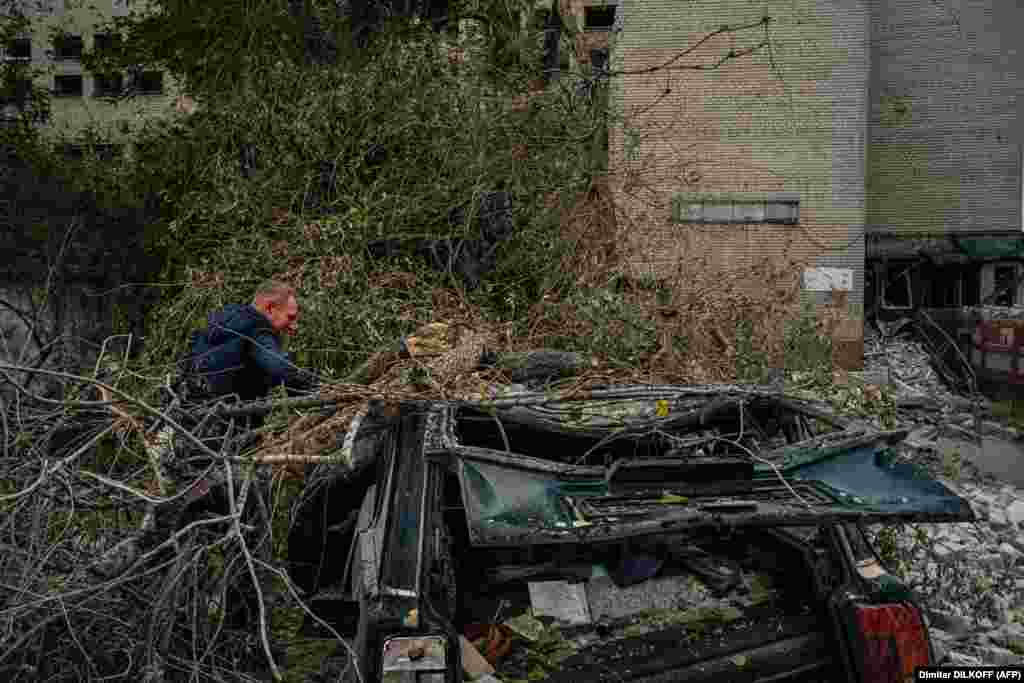 Egy helyi férfi egy fa által összezúzott autót vizsgál