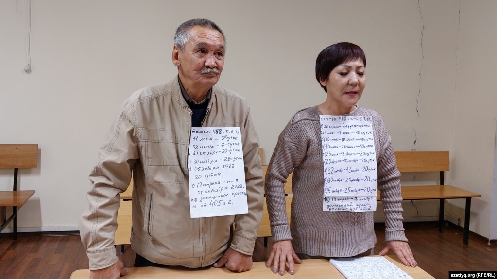 Гражданские активисты Маруа Ескендирова и Амангельды Оразбаев на суде по их делу с плакатами, на которых перечислены сутки, в которые они в разное время отбывали административные аресты. Уральск, 7 октября 2022 года