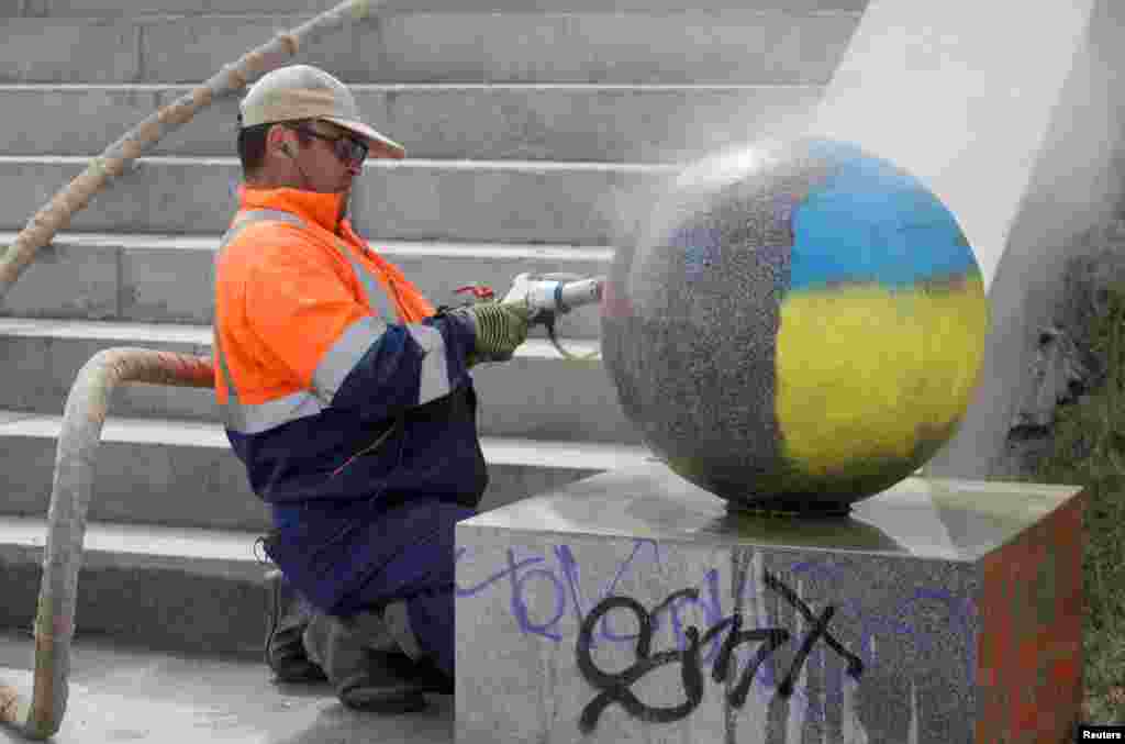 A worker cleans off paint in the colors of the Ukrainian flag from a decorative granite ball on an embankment of Yekaterinburg, Russia, on August 11.&nbsp;