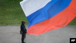 Az orosz belügyminisztérium rendőre őrködik az egyik választóhelyiség előtt, jobbján orosz zászlóval az úgynevezett Luhanszki Népköztársaságban az annektálásról szóló referendum idején Luhanszkban 2022. szeptember 27-én