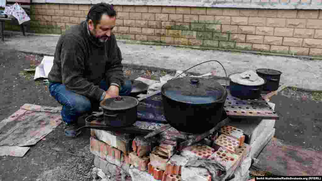 Місцевий житель готує їжу на відкритому вогні біля бомбосховища, на одній з вулиць Сєвєродонецька, 16 квітня 2022 року&nbsp;