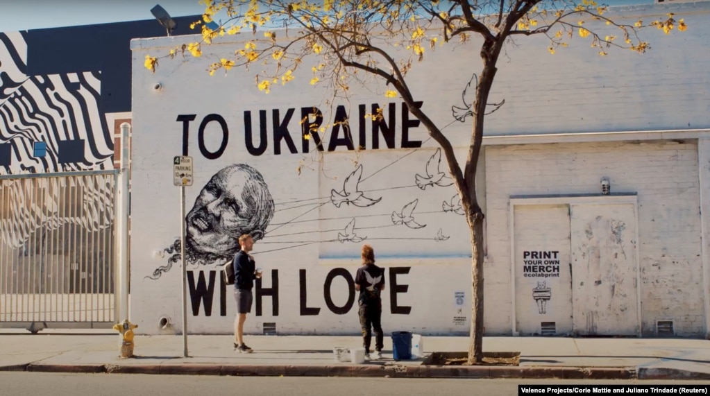 Artistët Juliano Trindade dhe Corie Mattie nga Valence Projects duke qëndruar para muralit që kanë realizuar së bashku, të titulluar &ldquo;Ukrainës, me dashuri&rdquo;, në Los Anxhelos, SHBA, më 8 maj. Mattie ka thënë për Radion Evropa e Lirë se ishte e rëndësishme të shfaqej një shenjë shprese, me pëllumbat që ia merrnin fuqinë Putinit. &ldquo;Unë mendoj se të gjitha format e artit mund të bëjnë dallimin&rdquo;, është shprehur ajo. &ldquo;I shtyn shikuesit të mendojnë për situatat aktuale, t&rsquo;i ndryshojnë pikëpamjet, e madje edhe të veprojnë&rdquo;. Ky mural ka një kod QR, i cili të çon te banka kombëtare e Ukrainës, e cila ka themeluar një fond për të mbledhur para për trupat ukrainase. &ldquo;Është e rëndësishme që njerëzve t&rsquo;ju ofrohet qasje në aktivizëm&rdquo;, ka thënë Mattie. &ldquo;Arti i mirë të bën të mendosh, por arti i mrekullueshëm të bën të veprosh&rdquo;.