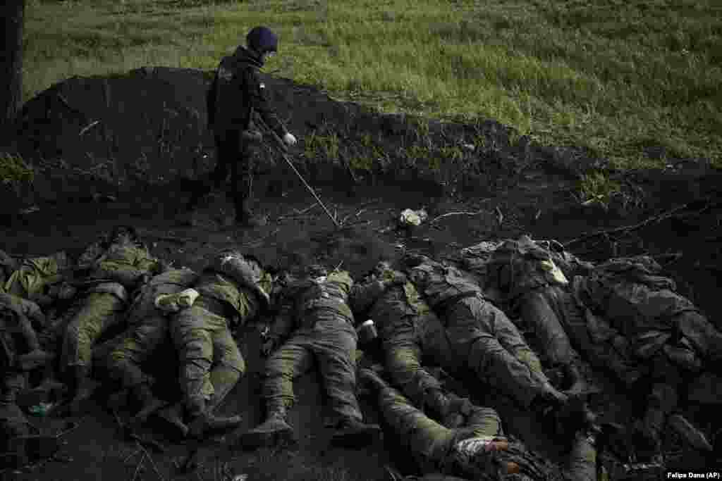 A member of a demining team checks for explosives around the bodies of 11 Russian soldiers in the village of Vilkhivka, near Kharkiv, which was recently retaken by Ukrainian forces.