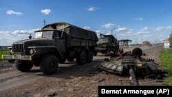 Ukrán katonai járművek haladnak el egy megsemmisített orosz tank darabjai mellett Harkiv északi részén 2022. május 13-án