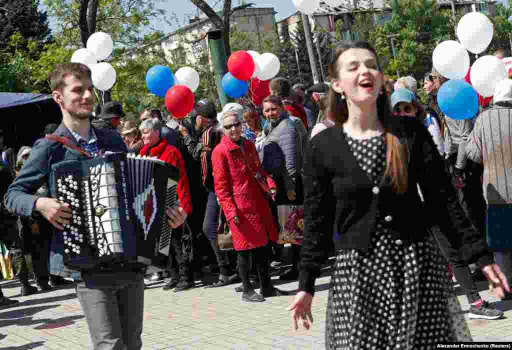 O mică mulțime se uită la spectacolul unor interpreți bine îmbrăcați.&nbsp;