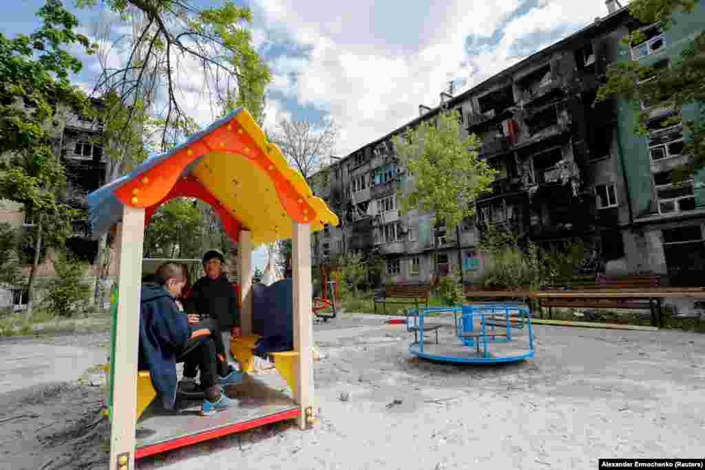 Fëmijët duke luajtur në një shesh lojërash, para ndërtesave të shkatërruara të banimit, më 11 maj.