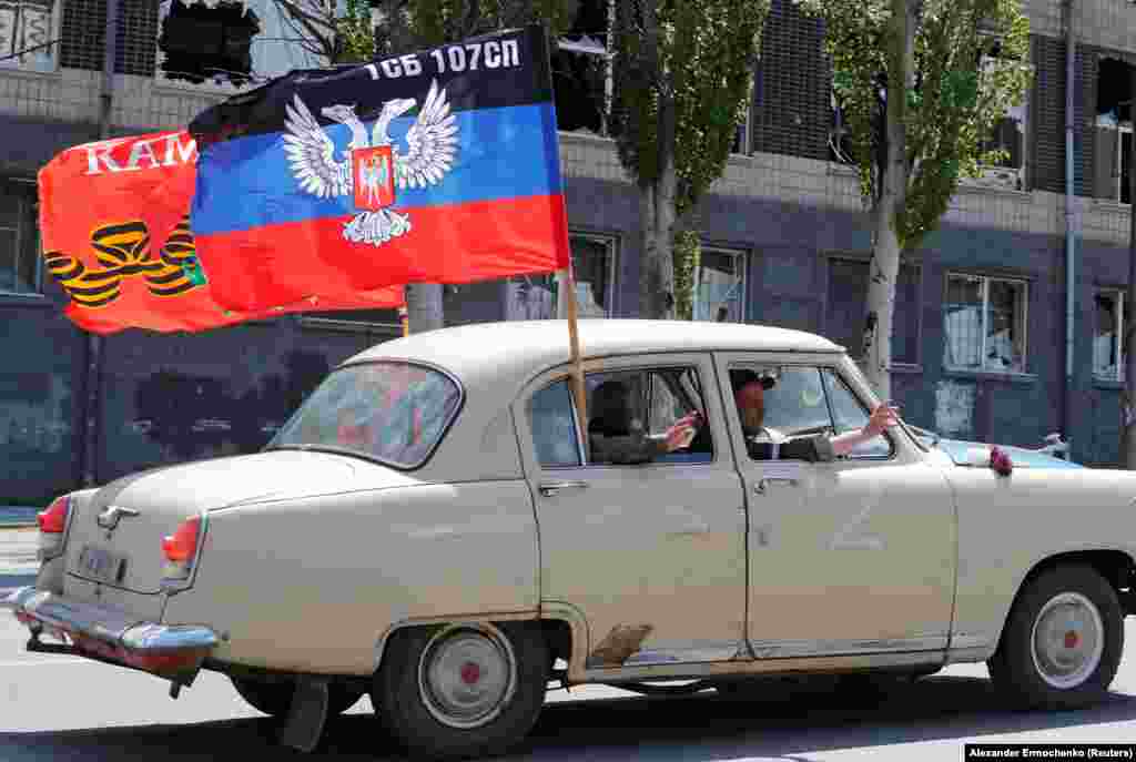 Separatist fighters wave from a car as they drive by the celebration in occupied Mariupol.