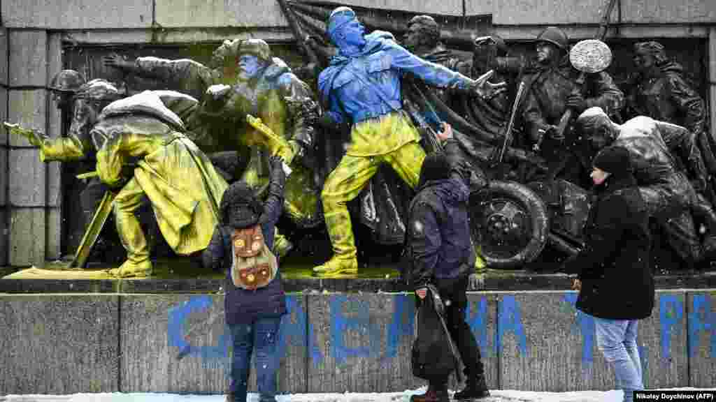 Tineri vopsind cu spray un basorelief cu soldați sovietici în centrul Sofiei, la 27 februarie.