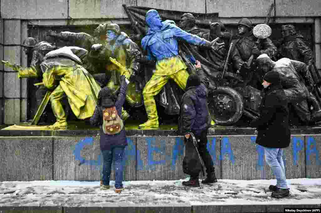 Un grup de tineri pictează cu spray mai multe statui a unor soldați sovietici într-un parc din centrul Sofiei, Bulgaria, 27 februarie 2022.