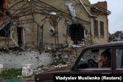 A resident sits in a car next to a destroyed house in Dolyna.