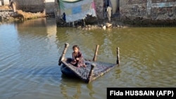 A girl sits on a cot as she crosses a flooded street in Balochistan Province on October 4.