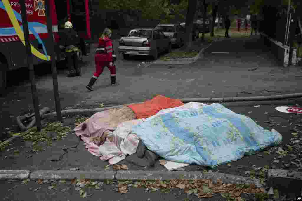 Pripadnica spasilačke službe prolazi pored tri tijela, pokrivena dekama, nakon ruskog napada u Dnjepru.