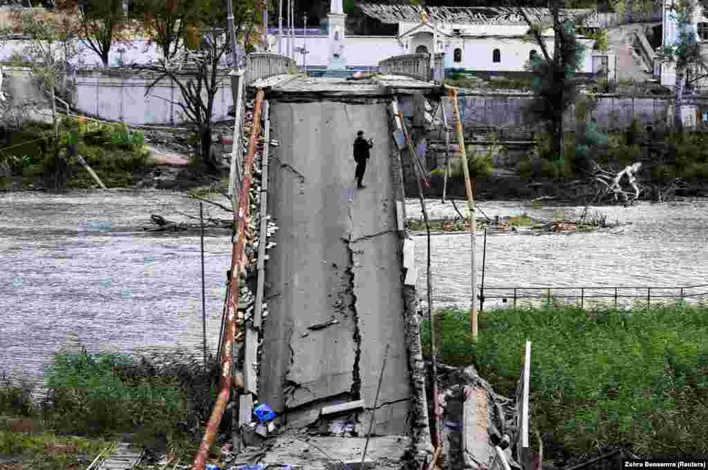 A man uses his mobile phone as he stands on a bridge destroyed by a Russian missile strike in Svyatohirsk, Ukraine.